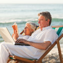 A senior man and woman recline on beach chairs reading books