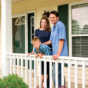 A young family standing on a porch of their home