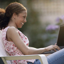 A young woman sits on a lawn chair and works on her computer