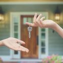 Image of a house key being passed from one hand to another in front of front door
