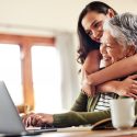 young woman hugging her grandmother before helping her with her finances on a laptop