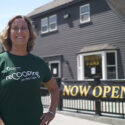 Coop Relationship Manager, Mary, wearing a ReCOOP tshirt, poses outside of small local business, Old Kings Coffeehouse