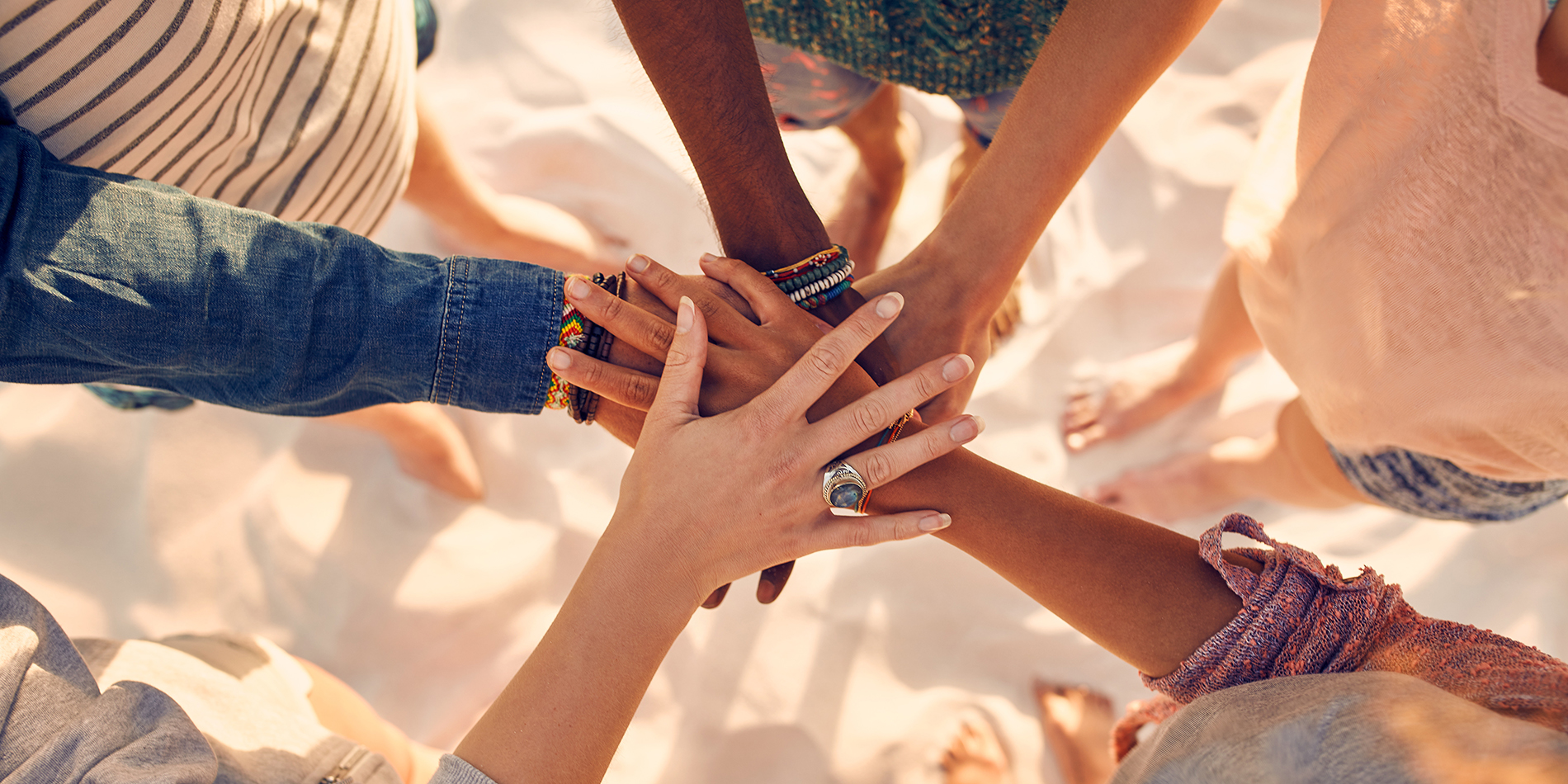 Closeup image of Group of mixed race friends on the beach with their hands stacked.